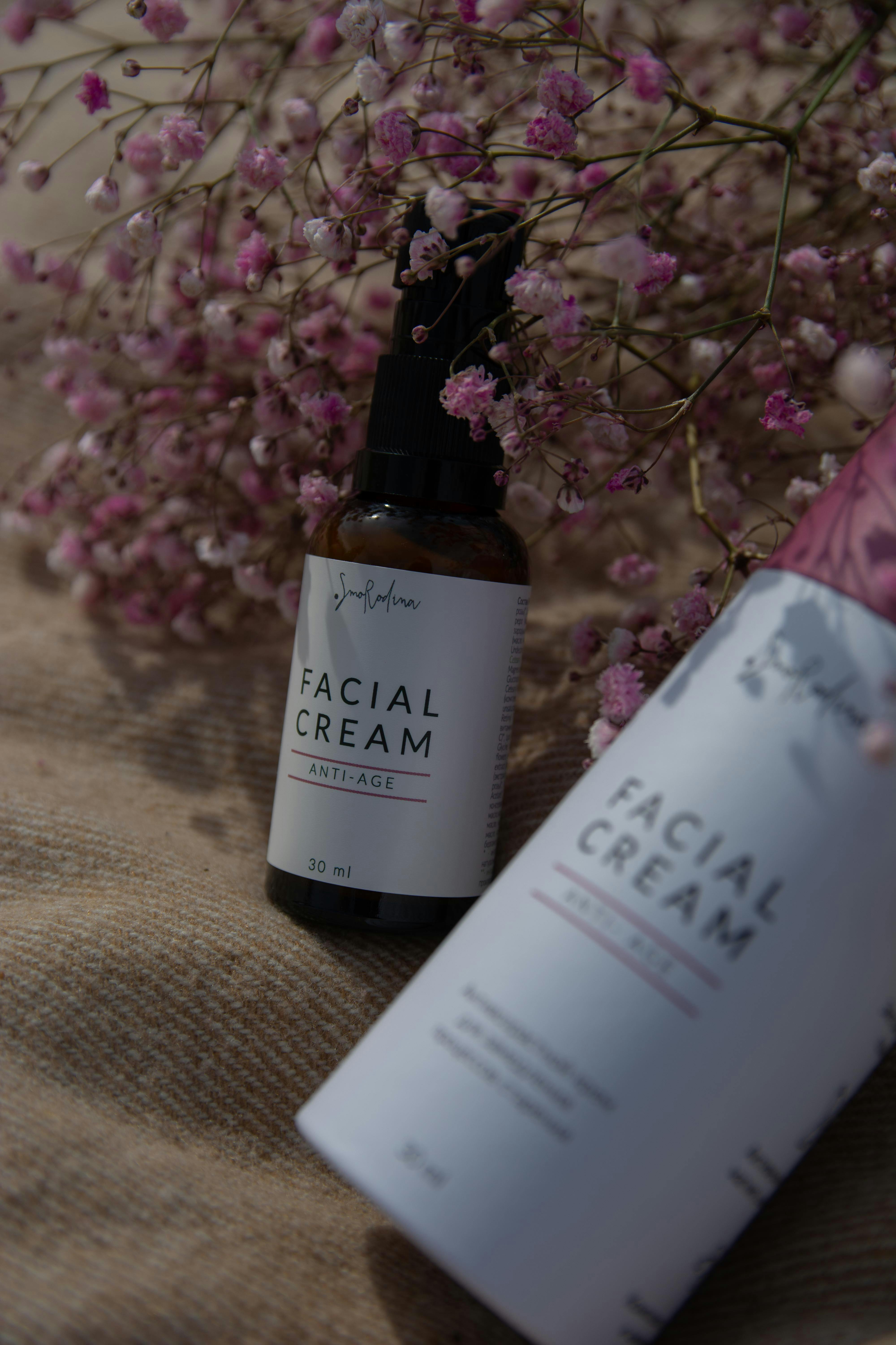 Two bottles of facial cream with a background of pink flowers.