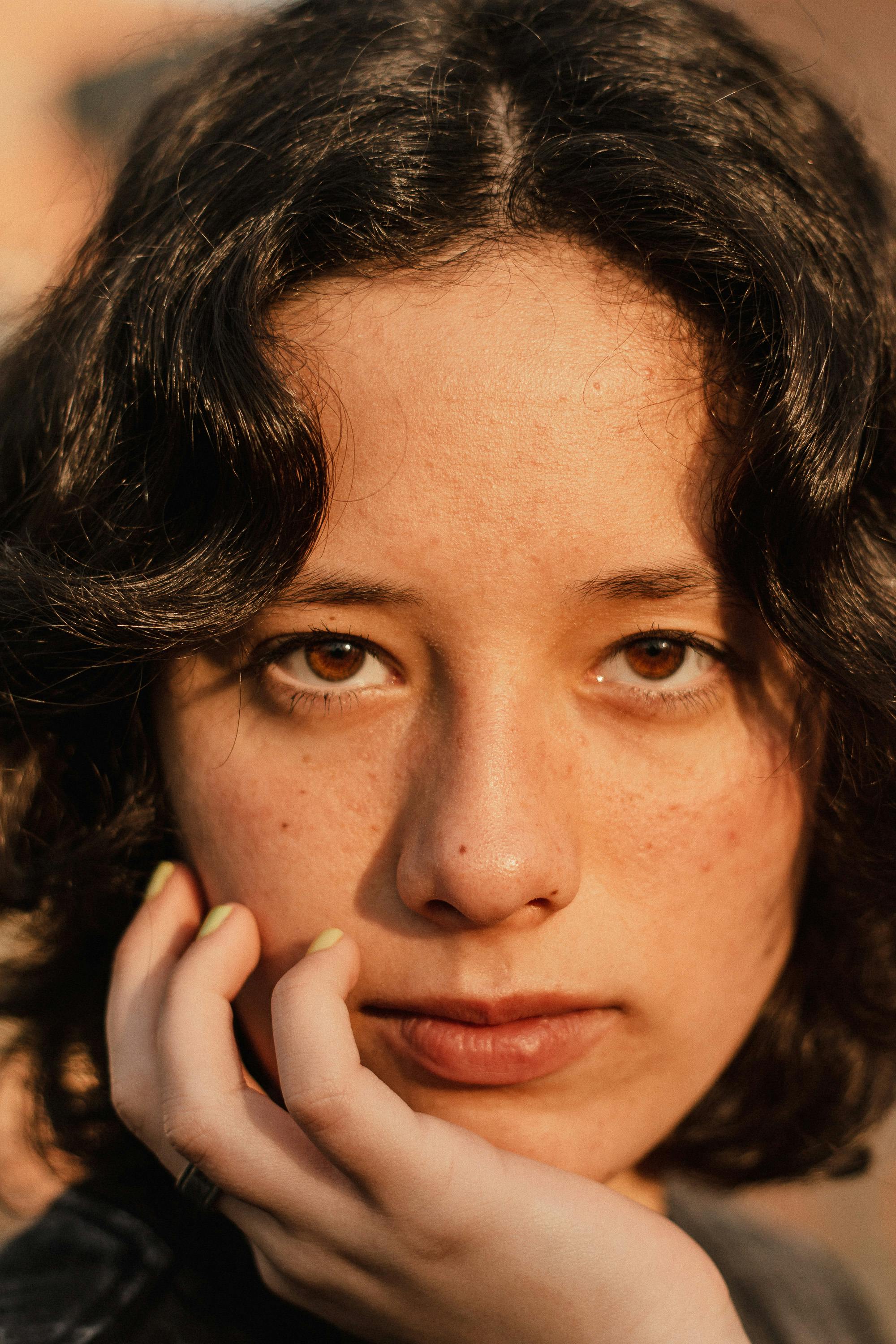 Close-up of a person with dark hair and freckles, wearing a black jacket.